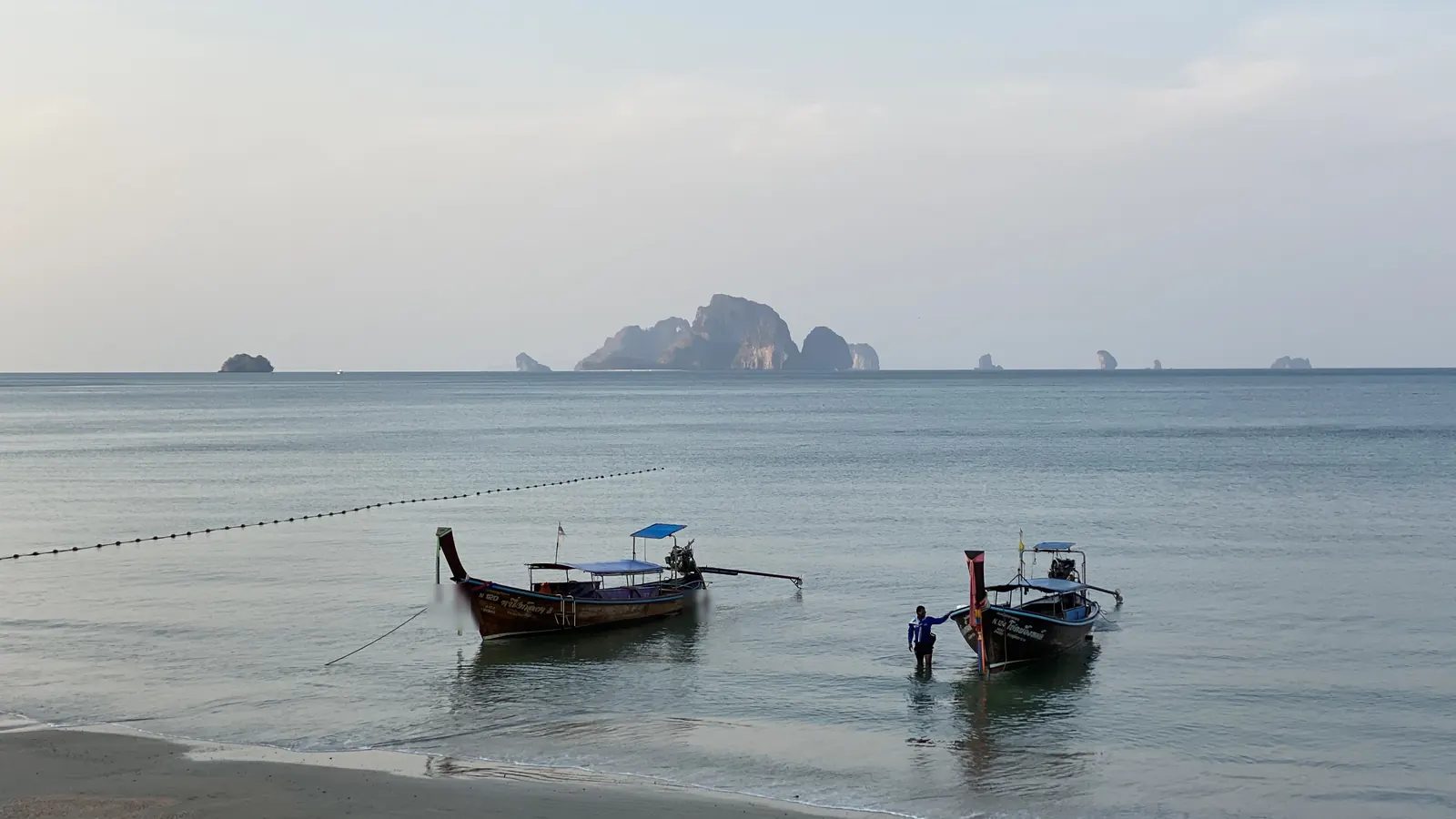 クラビの浜に係留されたロングテールボートと、沖に浮かぶ石灰岩の島